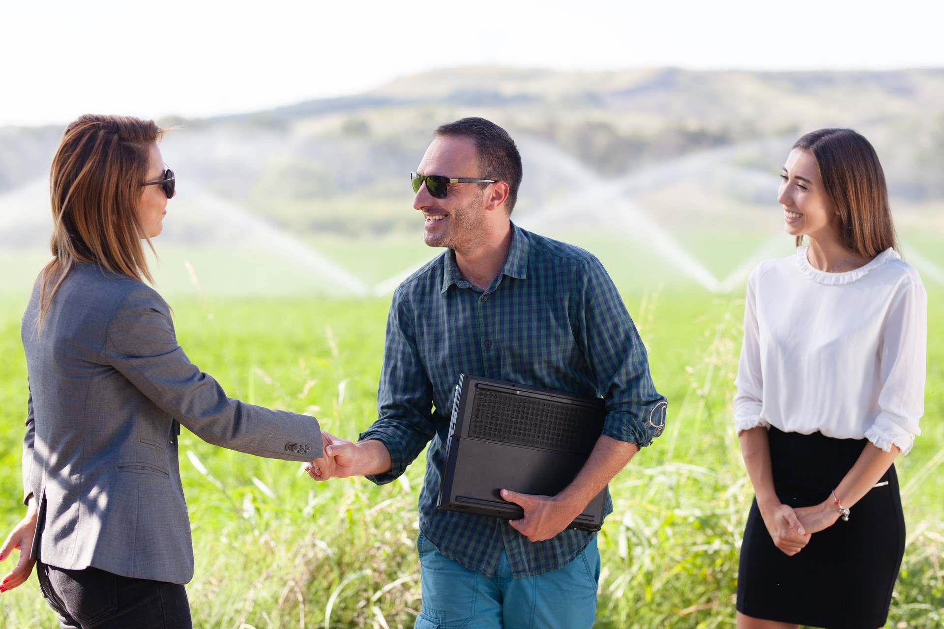 Business people shaking hands in a green field with agriculture irrigation system.